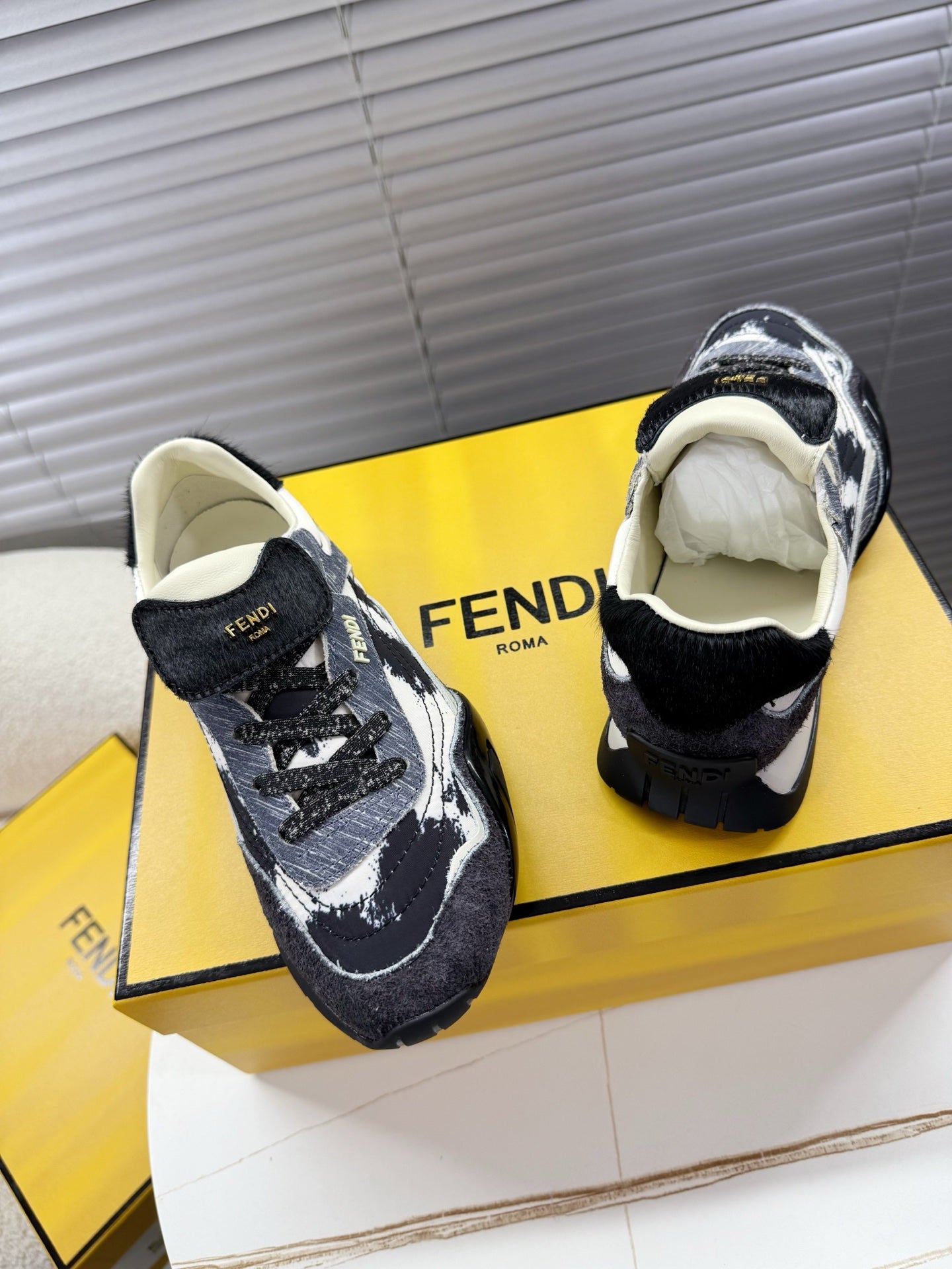 Fendi lace-up sneakers pair, black and white splatter, cream lining, close side view.