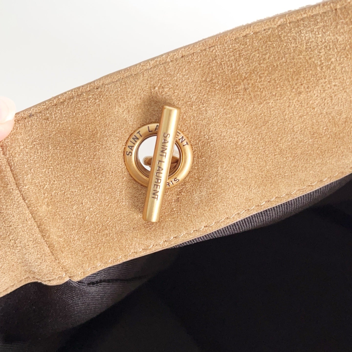 Tan suede pouch end detail with gold snap and circular logo emblem