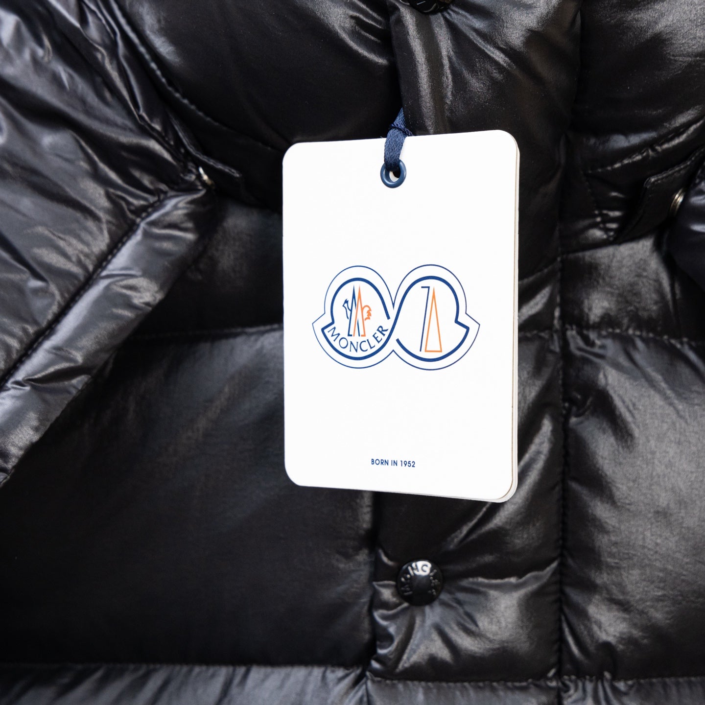 Moncler dark puffer jacket close-up, logo tag on buttoned chest pocket