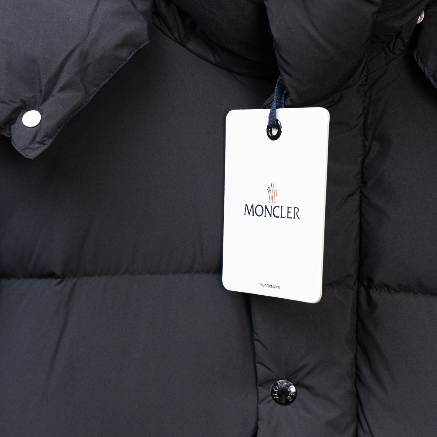 Moncler black puffer coat front with hanging white logo tag and snap button