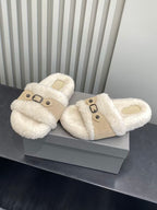 Pair of cream sherpa slide sandals with tan strap and black buckle detail