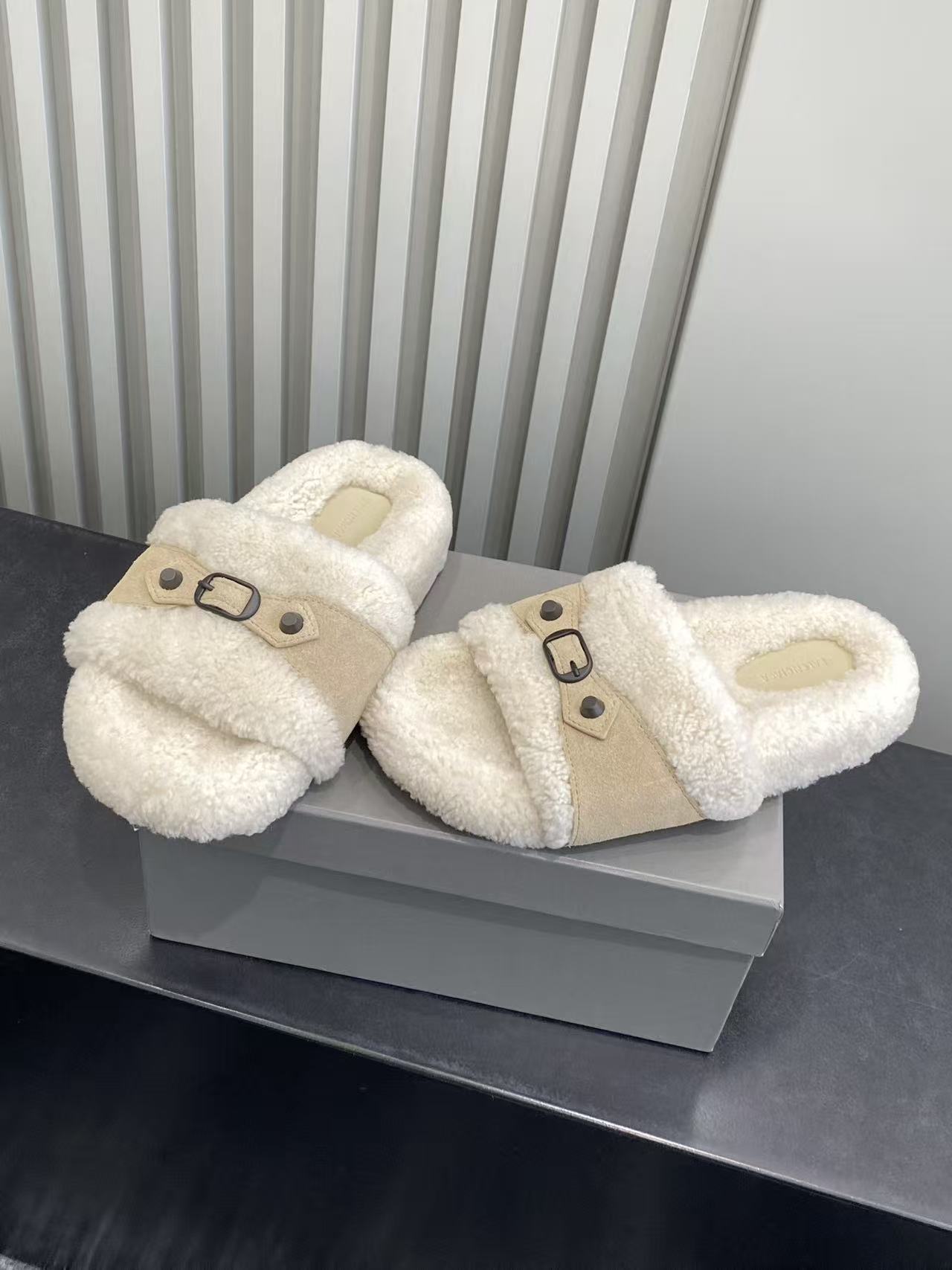 Pair of cream sherpa slide sandals with tan strap and black buckle detail