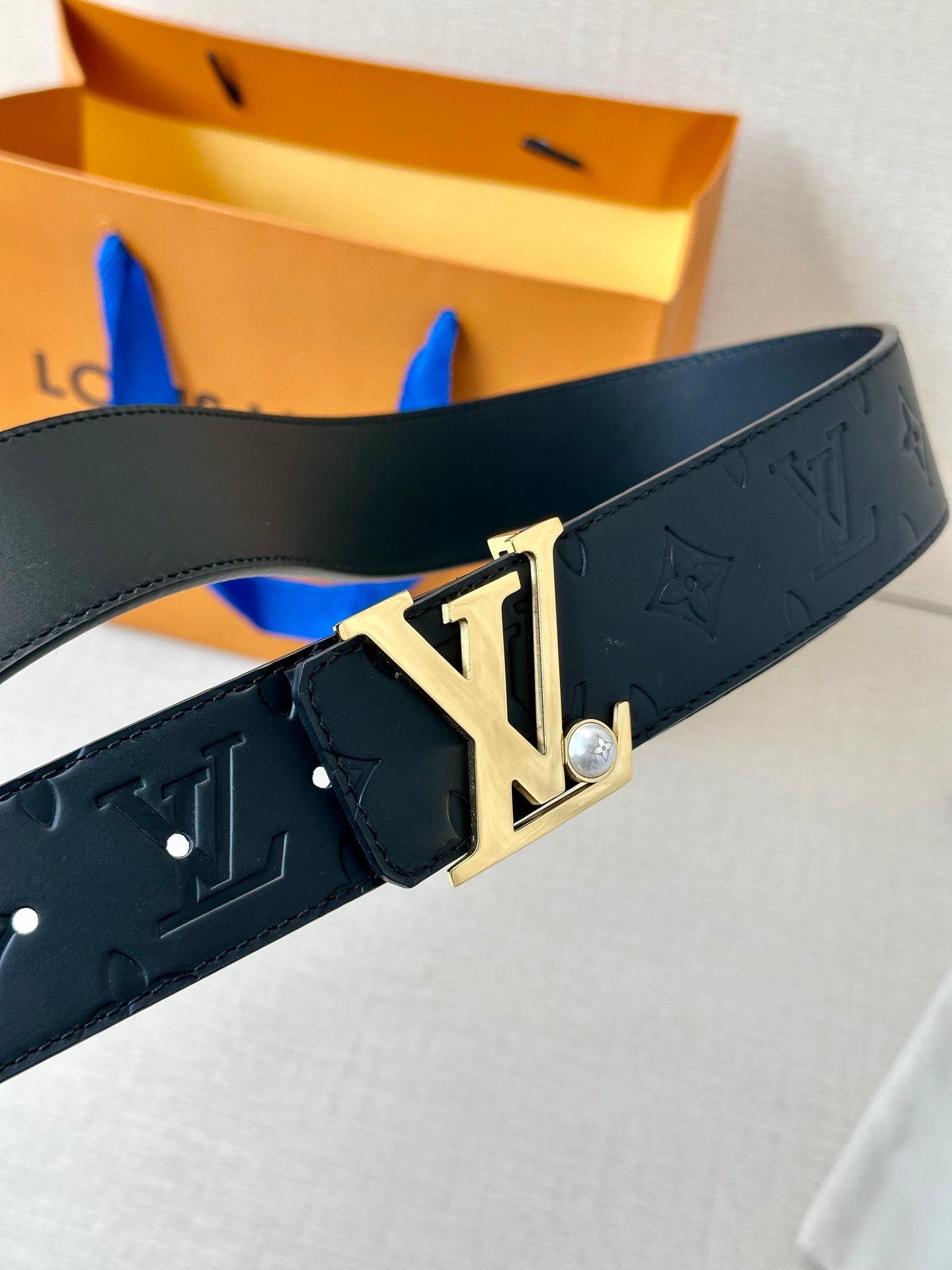 Dark monogram leather belt showing gold-tone LV buckle with small pearl detail.