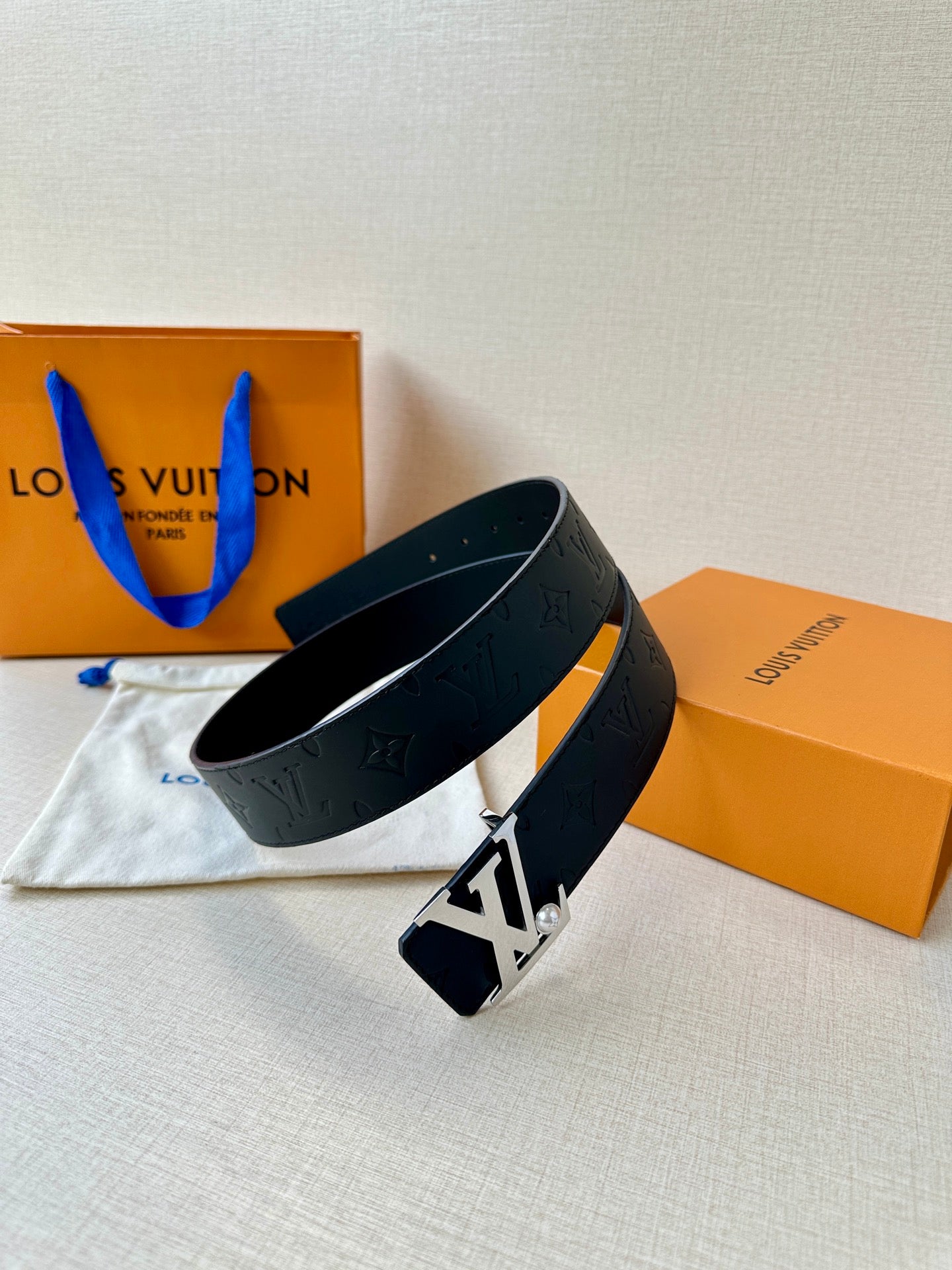 Dark leather belt with embossed monogram and gold-tone LV buckle, angled view.