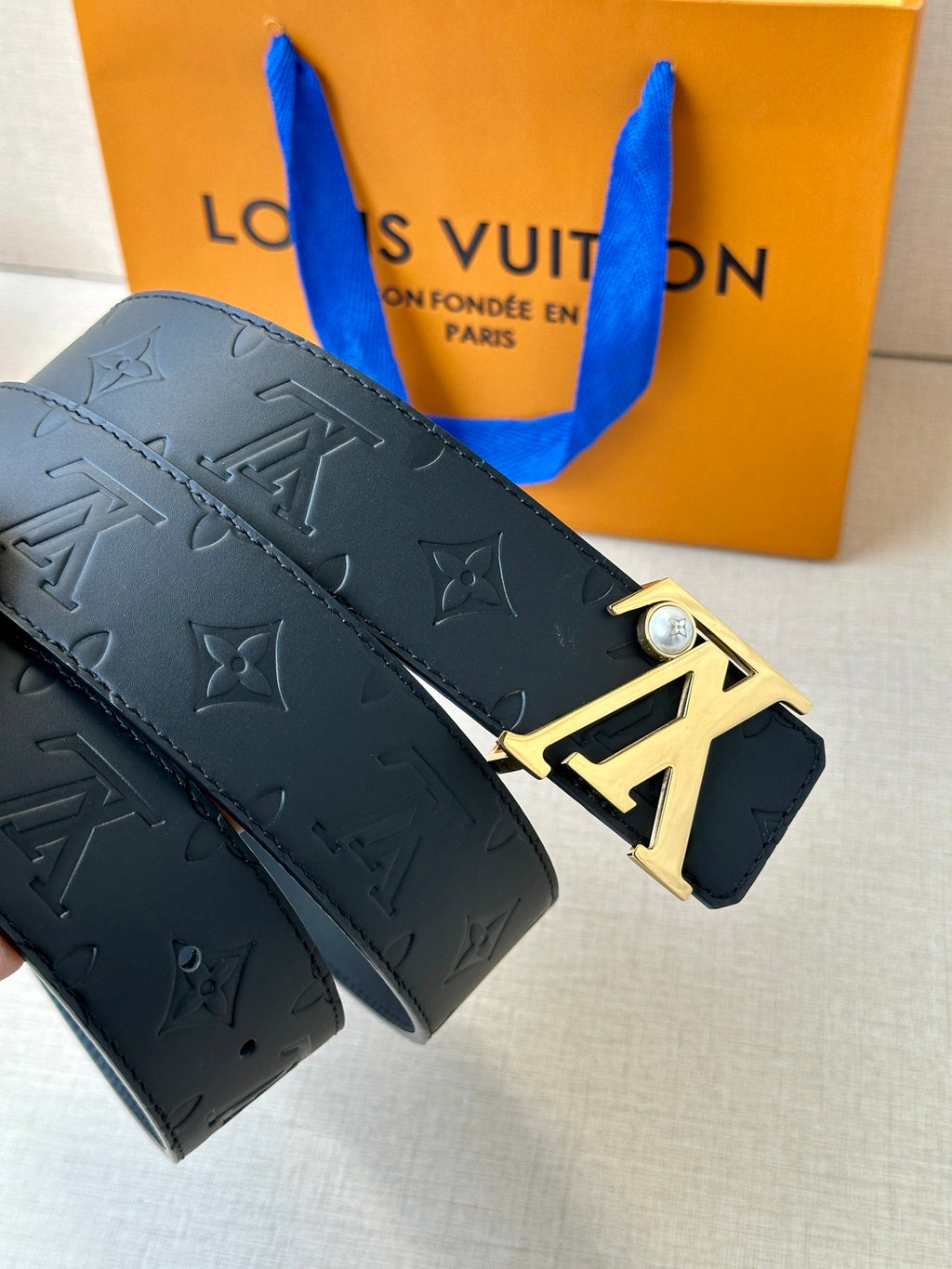 Dark leather belt with embossed monogram pattern and gold-tone LV buckle close-up.