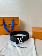 Dark leather belt with embossed monogram and gold-tone LV buckle on white dust bag.