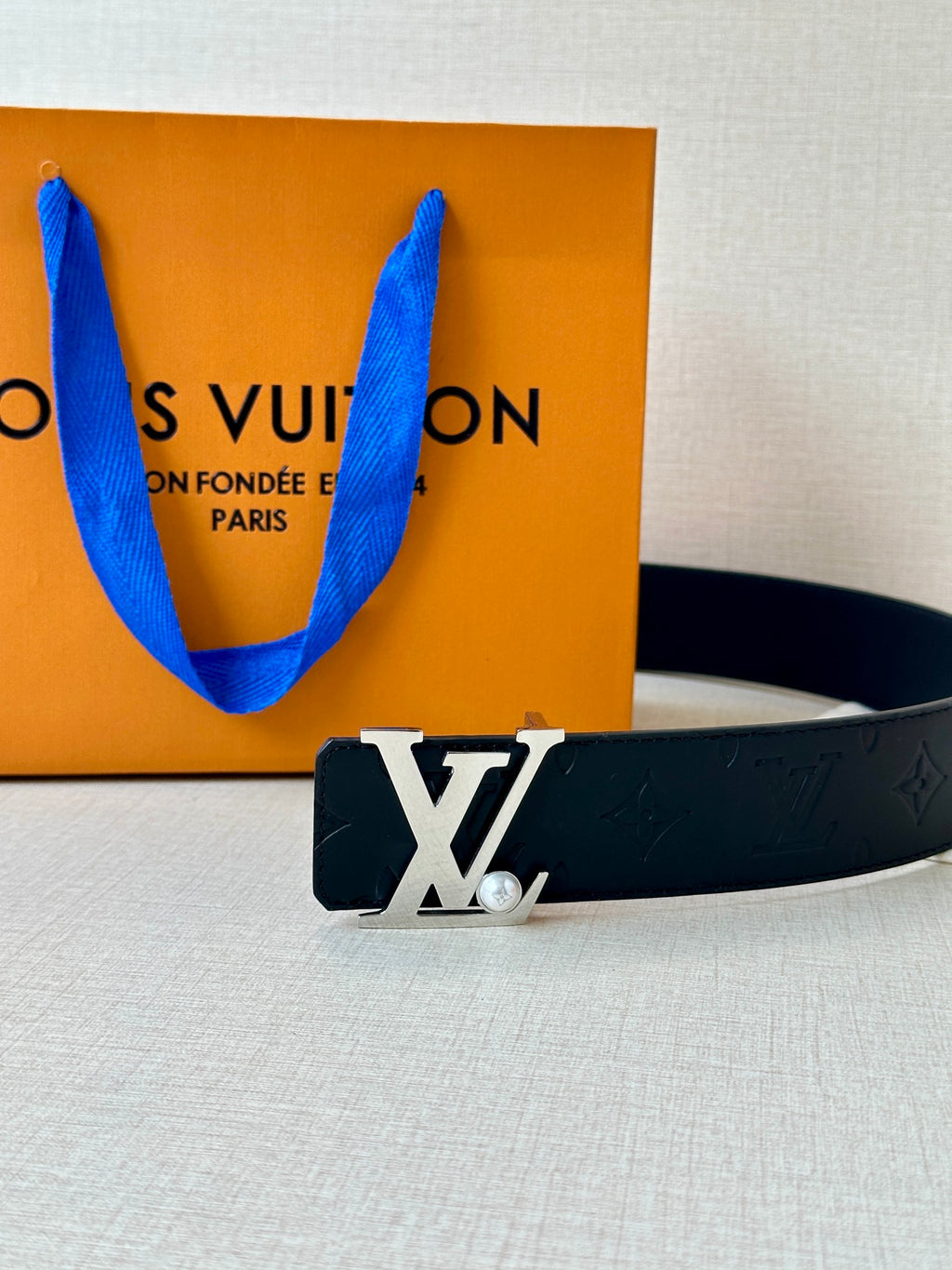 Dark leather belt with embossed monogram and gold-tone LV buckle on display surface.