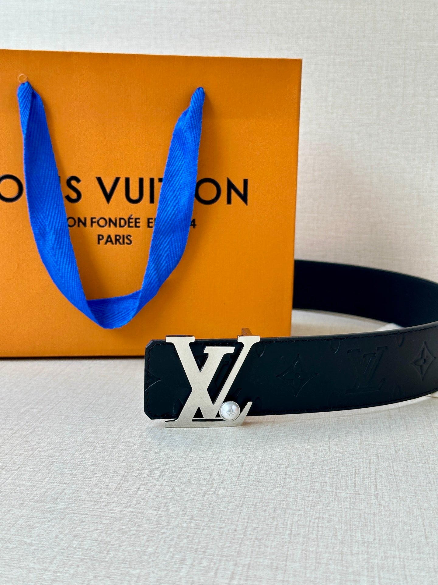 Dark leather belt with embossed monogram and gold-tone LV buckle on display surface.