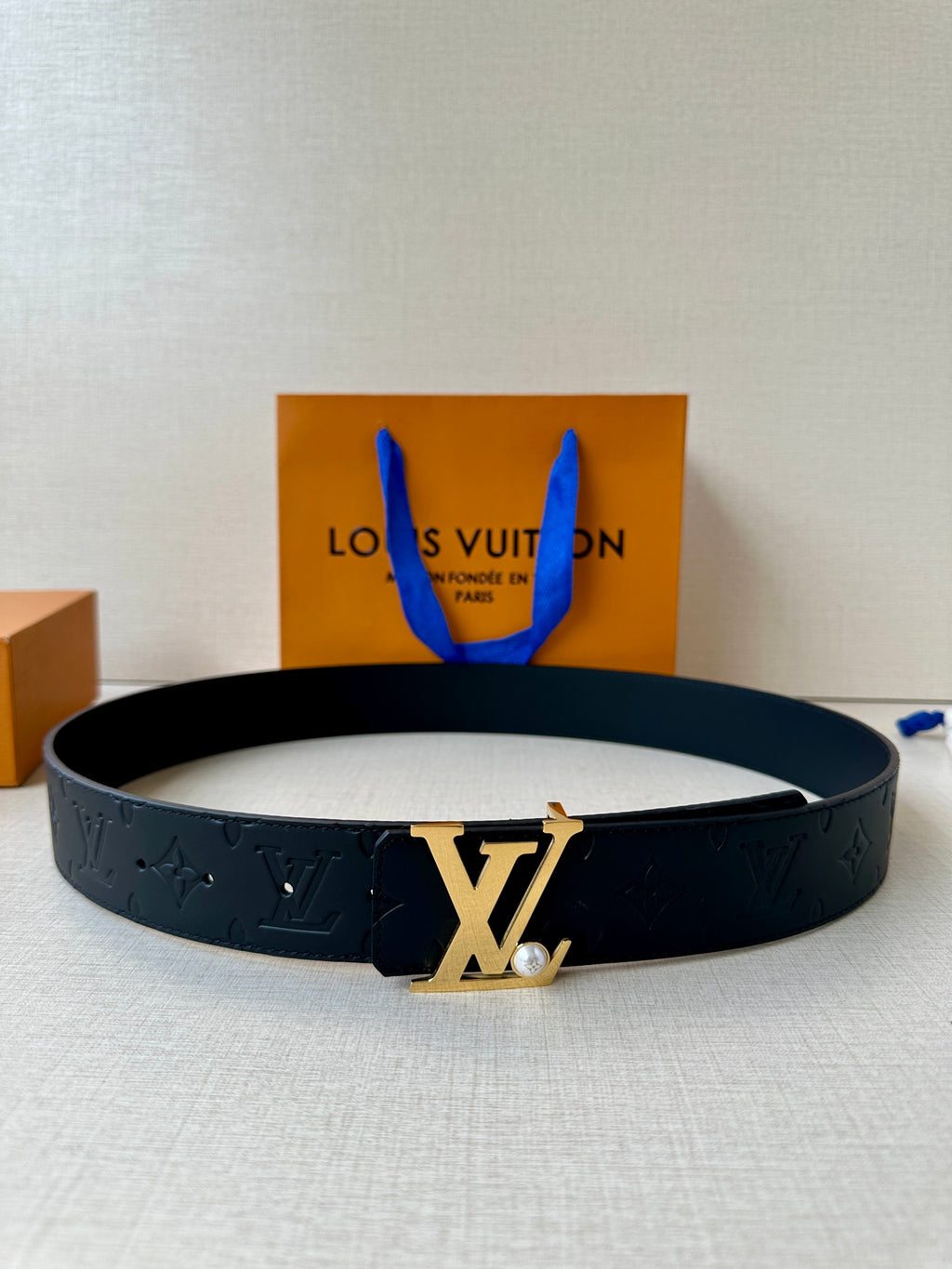 Dark leather belt with embossed monogram and gold-tone LV buckle on flat lay.