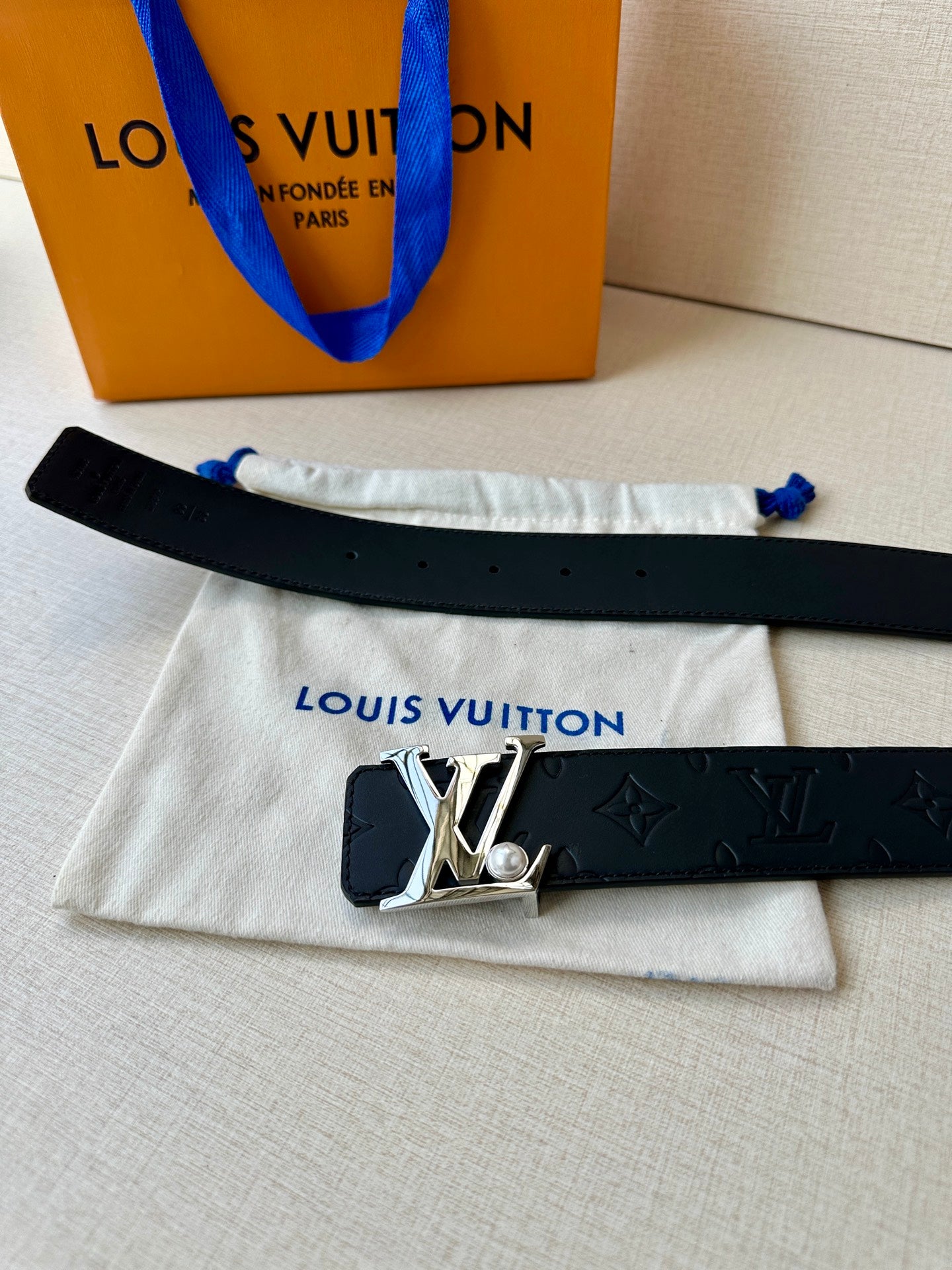 Dark leather belt with embossed monogram and gold-tone LV buckle on folded fabric.