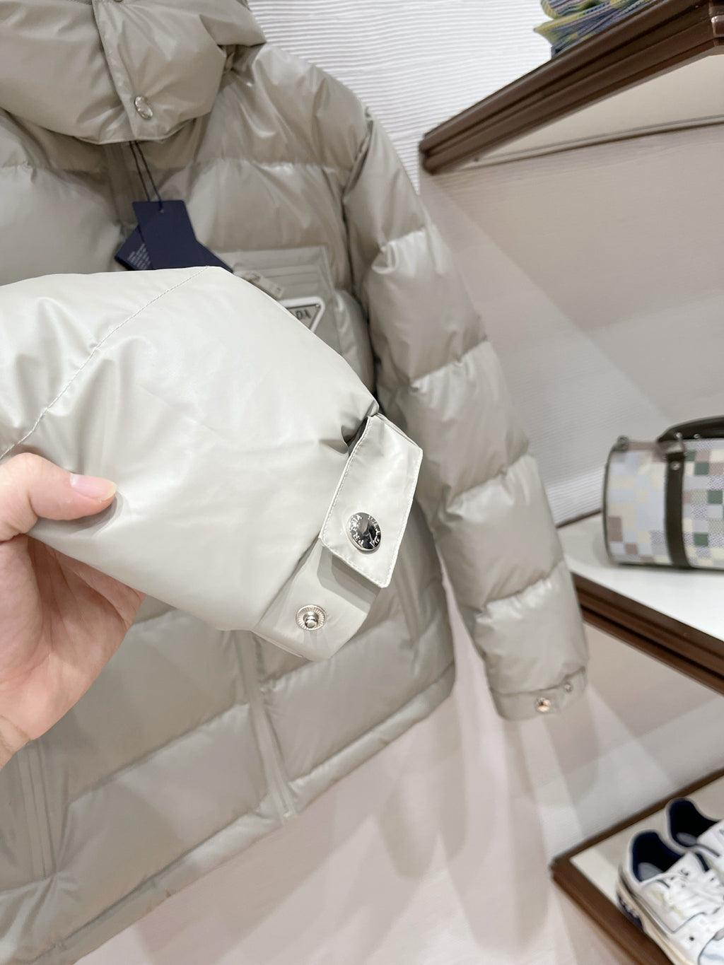 Long puffer jacket sleeve cuff in light beige with snap button and small logo emblem
