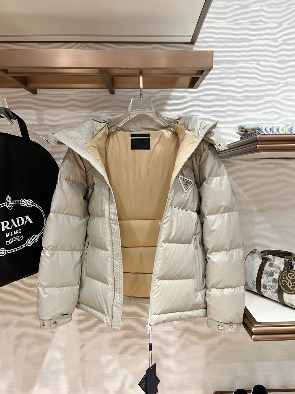 Long hooded puffer jacket in pale beige with quilted panels, front zipper, and hood snap buttons