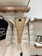 Long hooded puffer jacket in pale beige with quilted panels, front zipper, and hood snap buttons