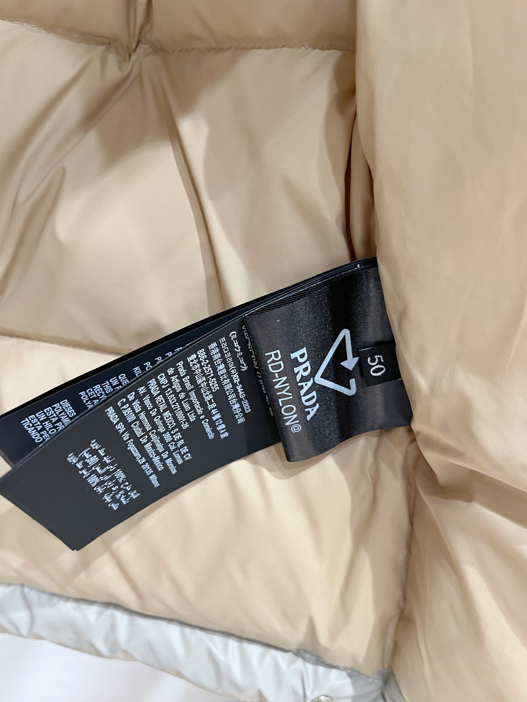 Interior fabric label in black on light beige puffer jacket, shows Prada and size 50