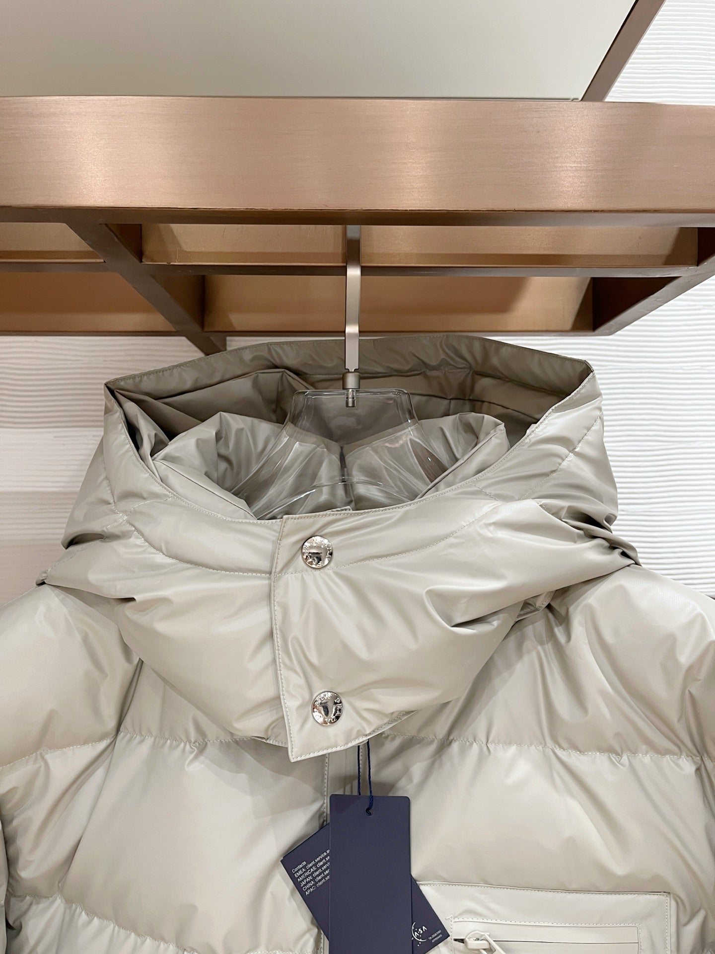 Long hooded puffer jacket in light beige with full-zip, snap buttons at the collar, logo detail