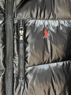 Black puffer jacket detail: center zip and red polo logo on chest panel