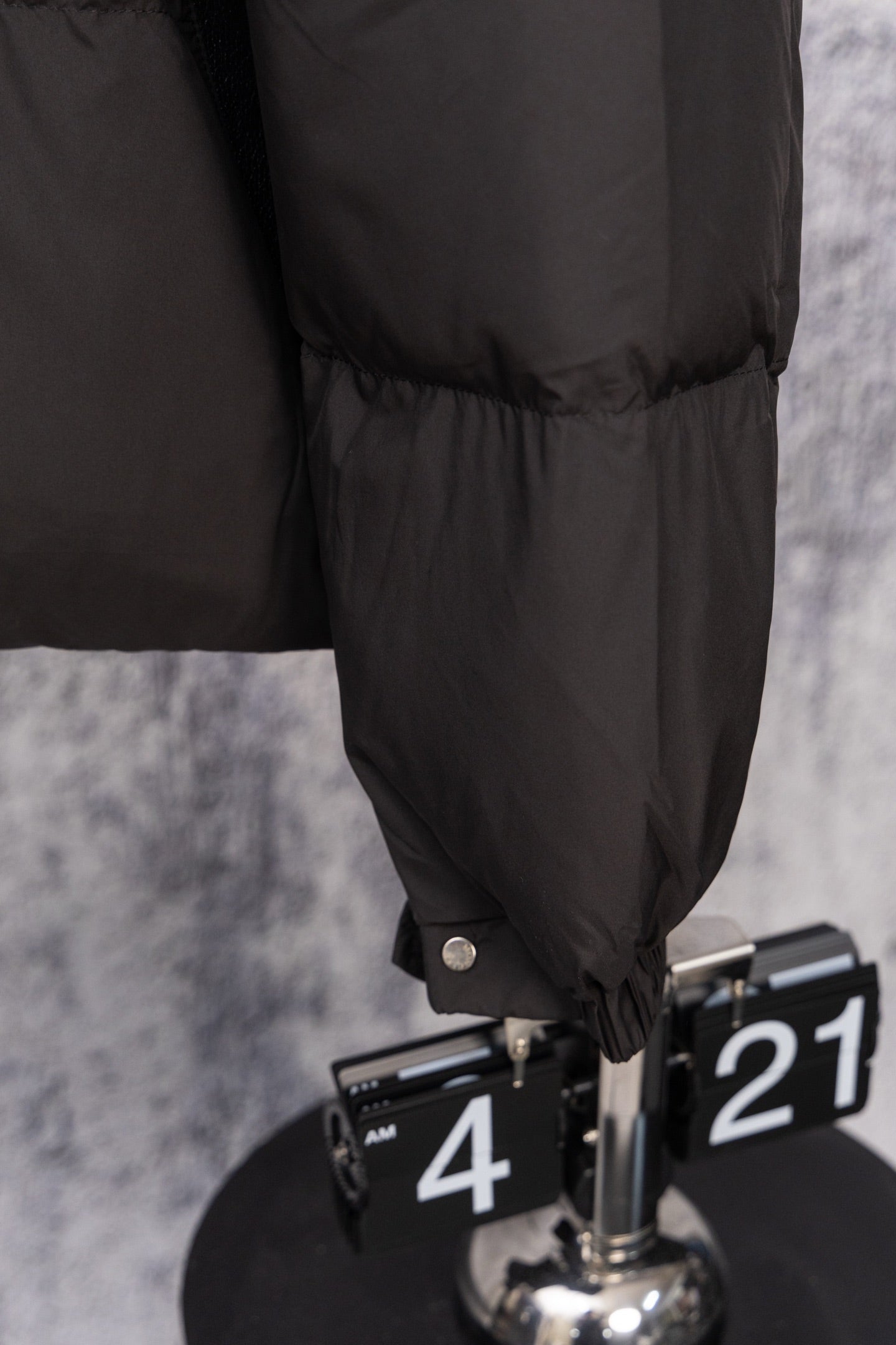 Long black puffer jacket hem with snap cuff detail