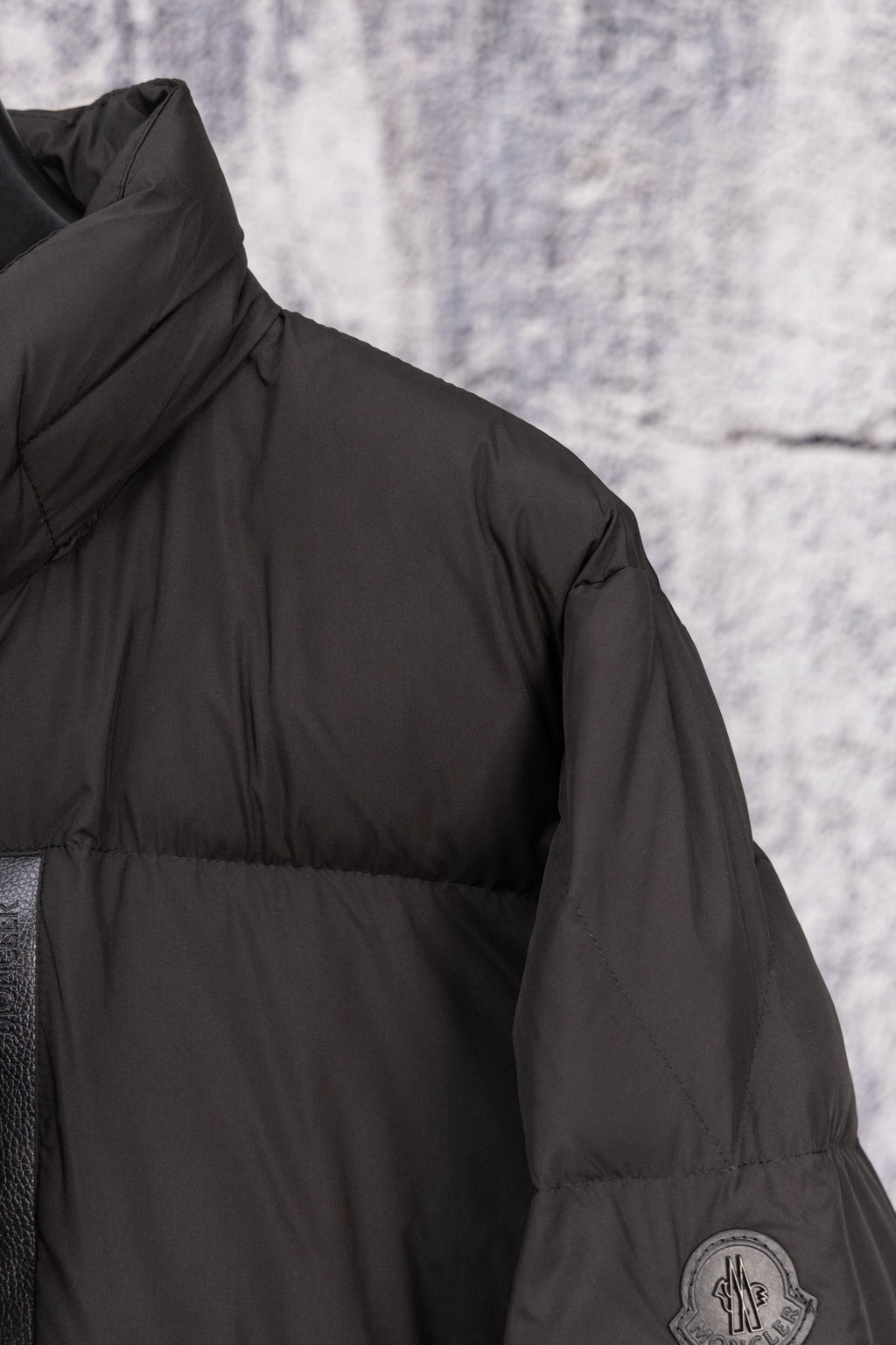 Long black puffer jacket shoulder seam with circular logo patch