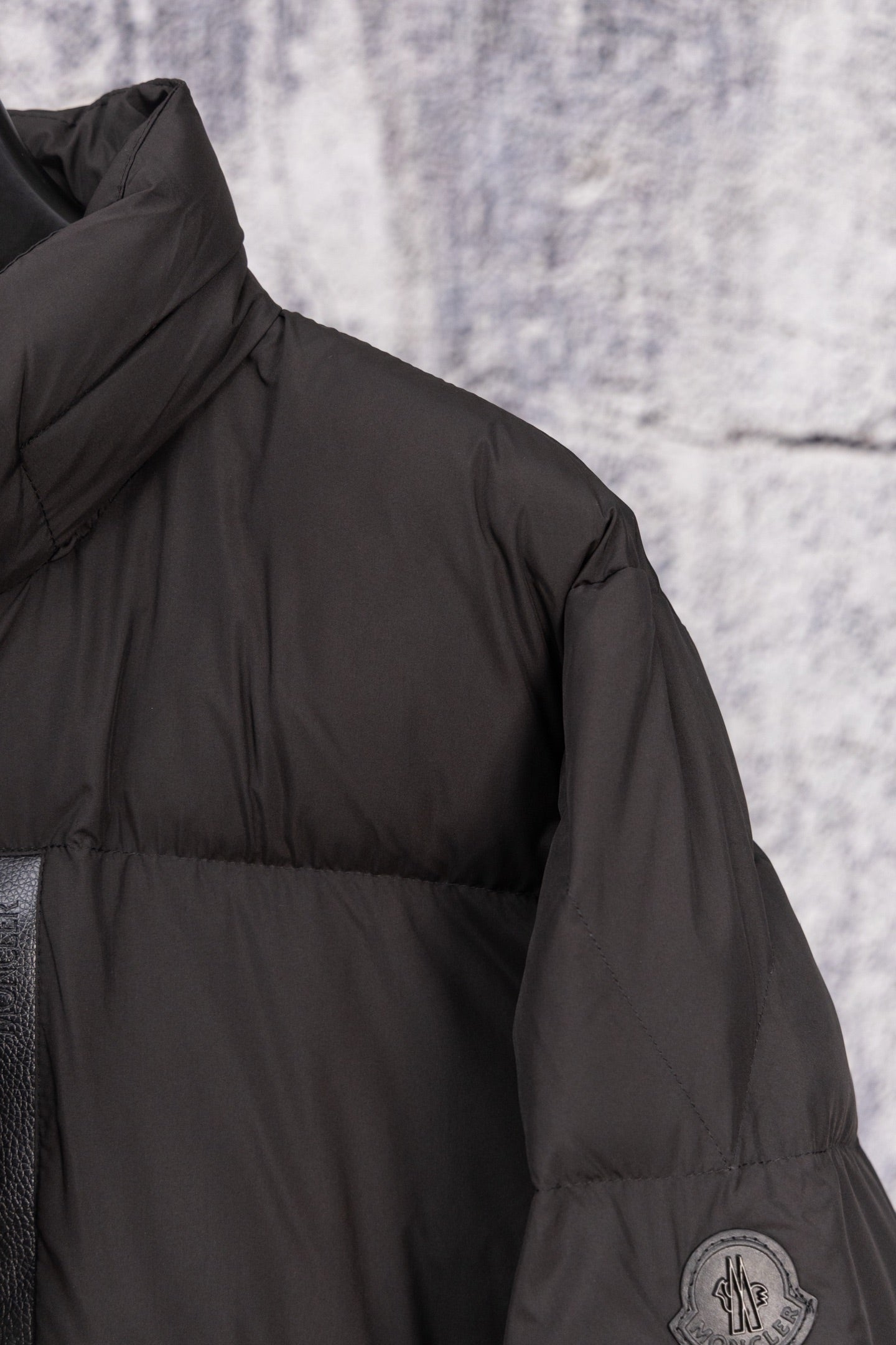 Long black puffer jacket shoulder seam with circular logo patch