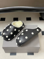 Black polka-dot slide clogs with white dots and plush shearling lining.