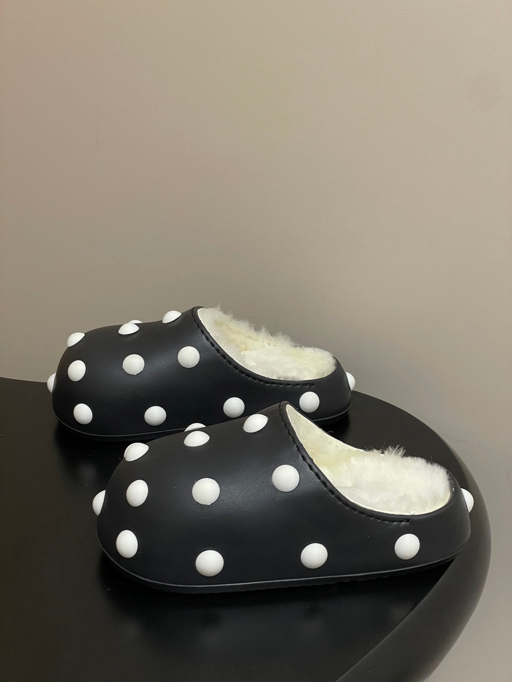Black polka-dot slide clogs with shearling lining, side-by-side view.
