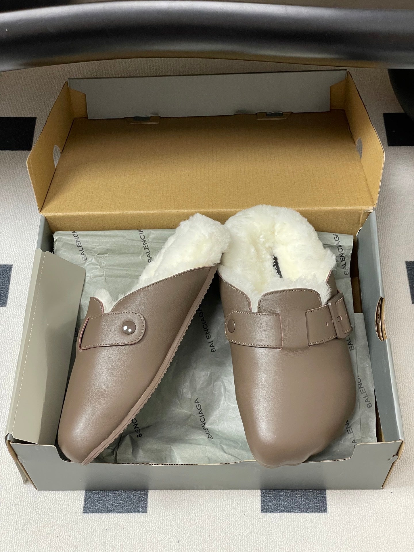 Taupe shearling-lined sandals in shoe box, angled pair with buckles.