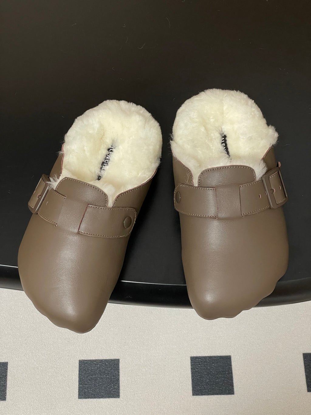 Taupe shearling-lined slide sandals with two-buckle strap detail.