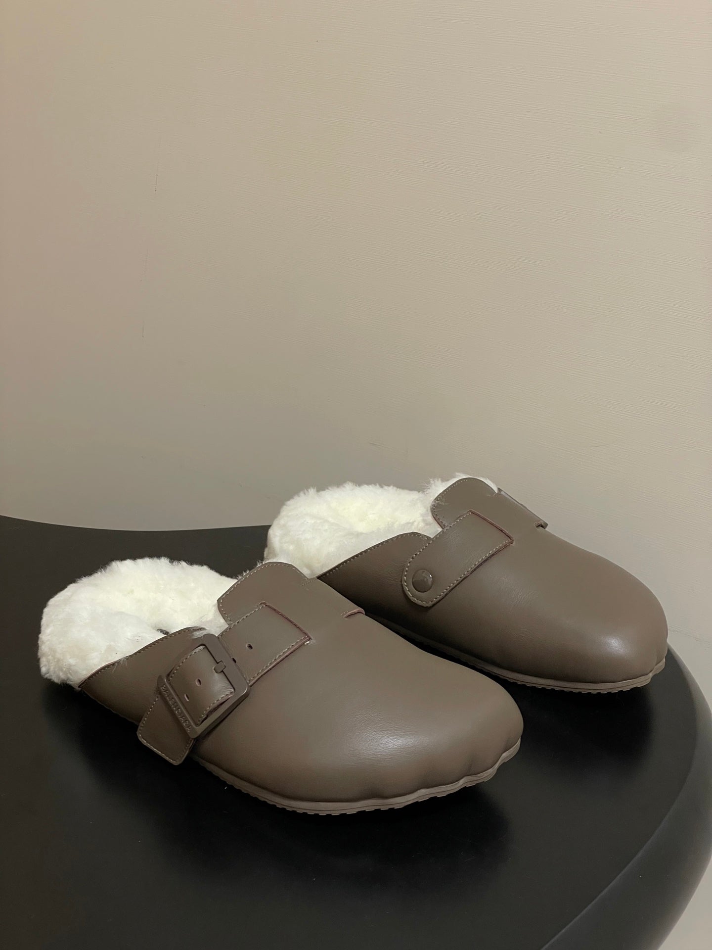 Taupe shearling-lined sandals with buckle strap and slip-on upper.
