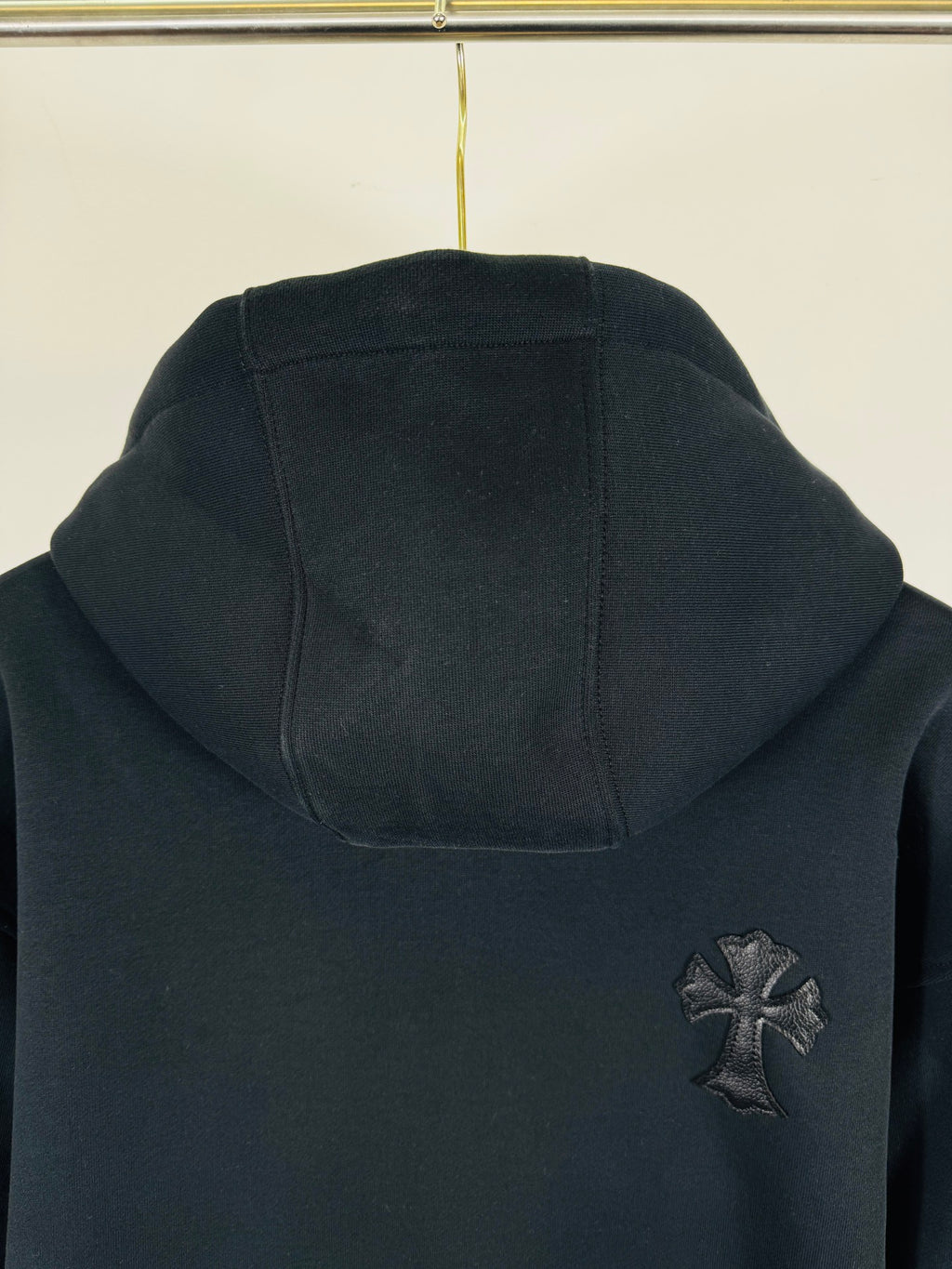 Black long-sleeve hoodie with front pocket and small cross chest patch