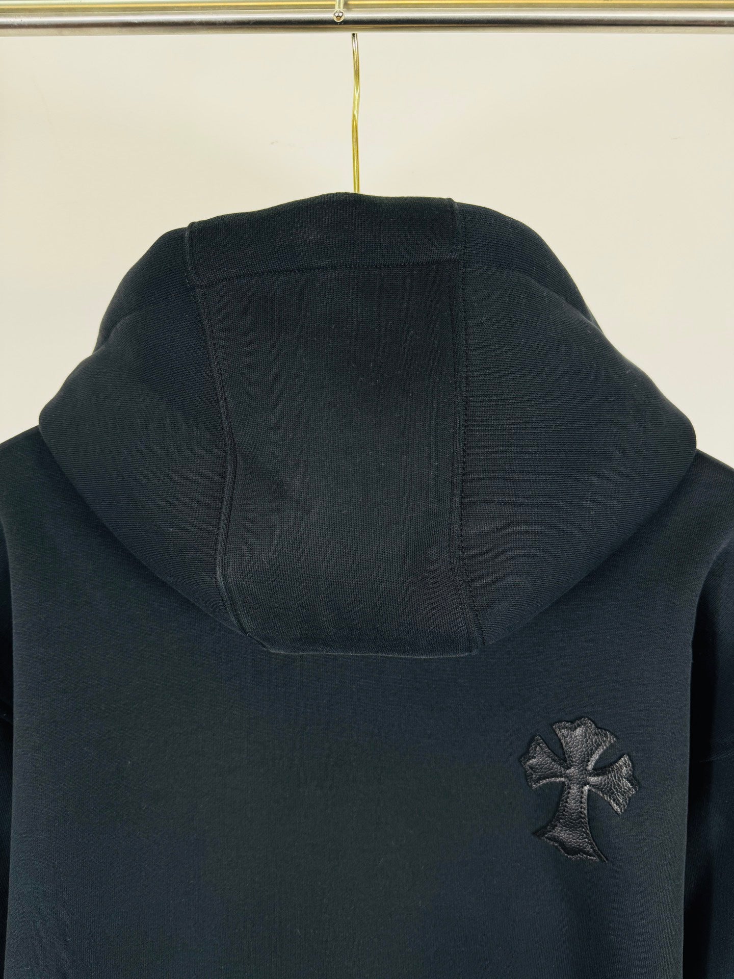 Black long-sleeve hoodie with front pocket and small cross chest patch