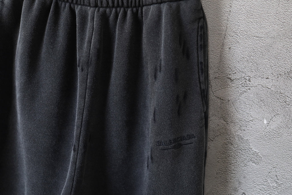 Black pants close-up showing side drape and small logo patch on leg
