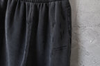 Black pants close-up showing side drape and small logo patch on leg