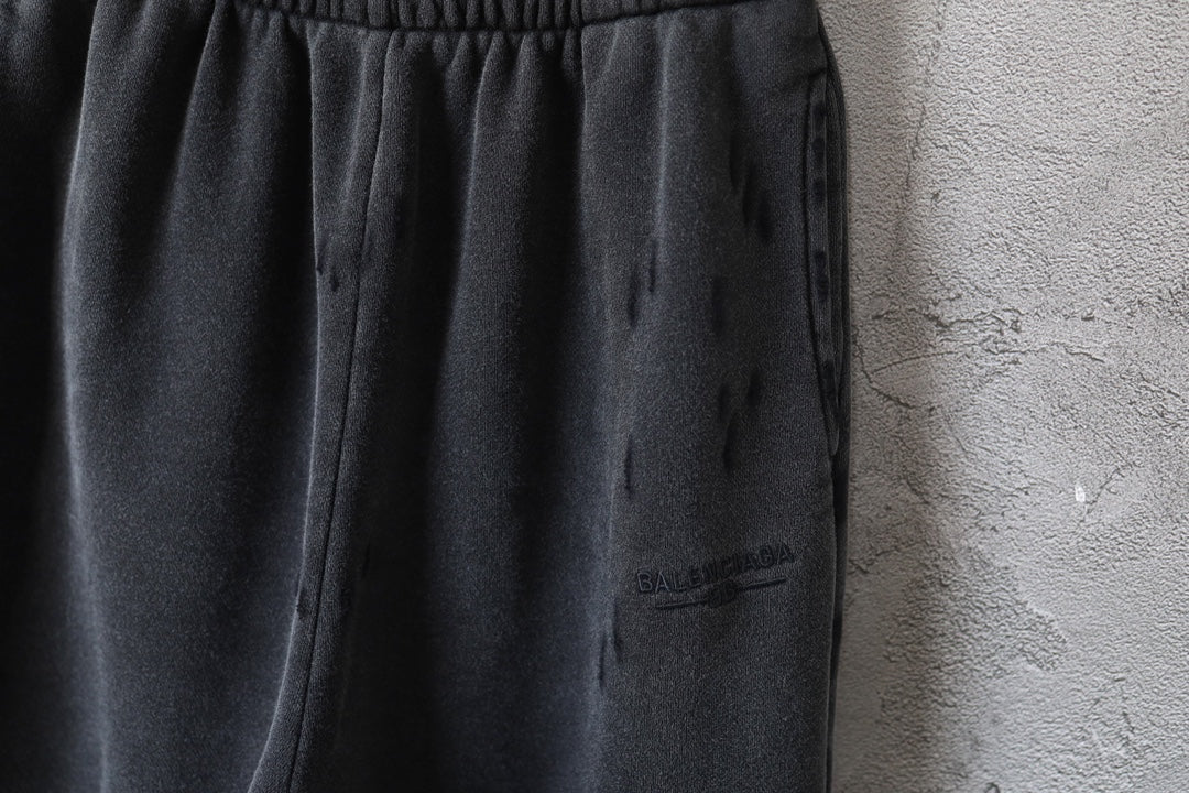 Black pants close-up showing side drape and small logo patch on leg