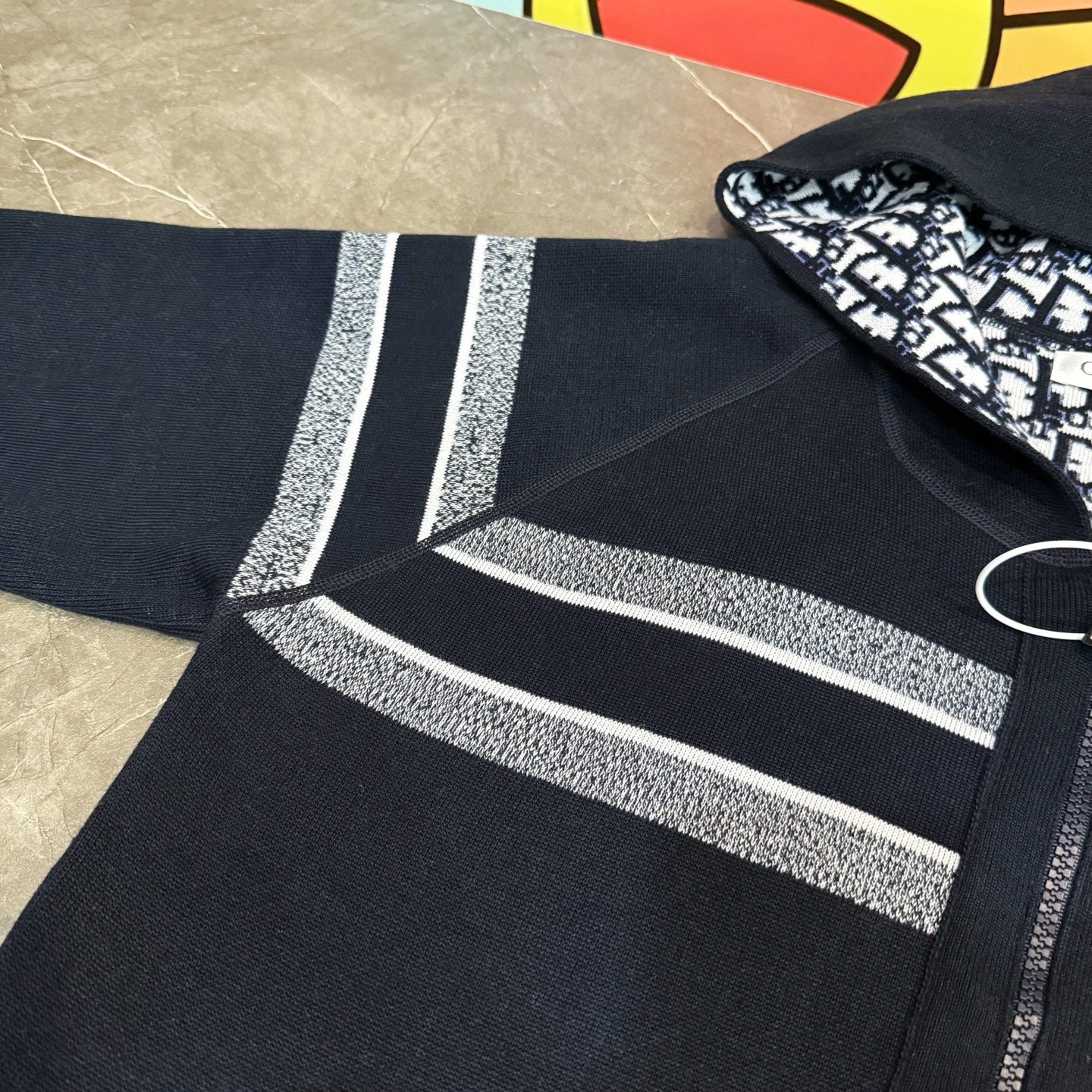 Navy zip hoodie sleeve with silver-gray logo stripe and textured knit