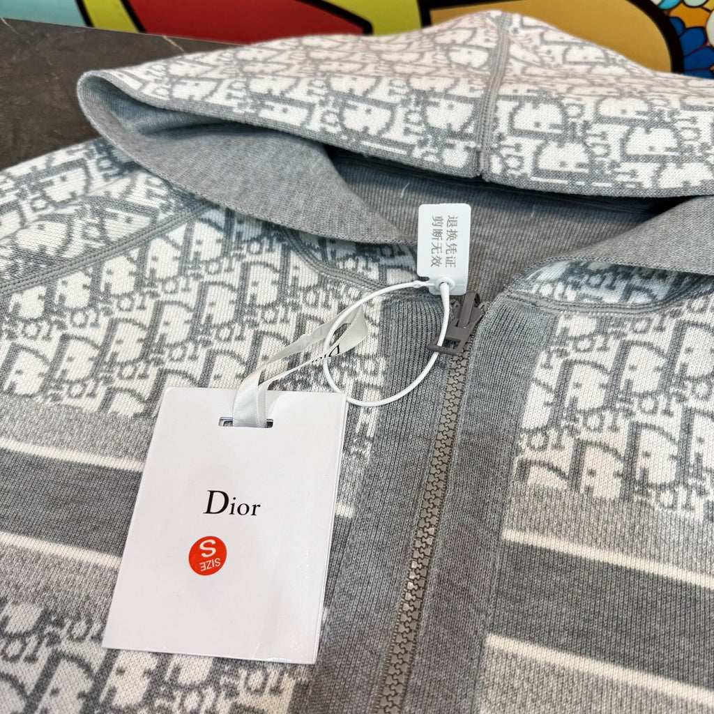 Close-up: gray and white monogram hooded sweatshirt fabric with Dior tag on zipper.