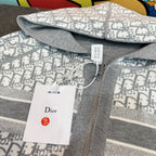 Close-up: gray and white monogram hooded sweatshirt fabric with Dior tag on zipper.