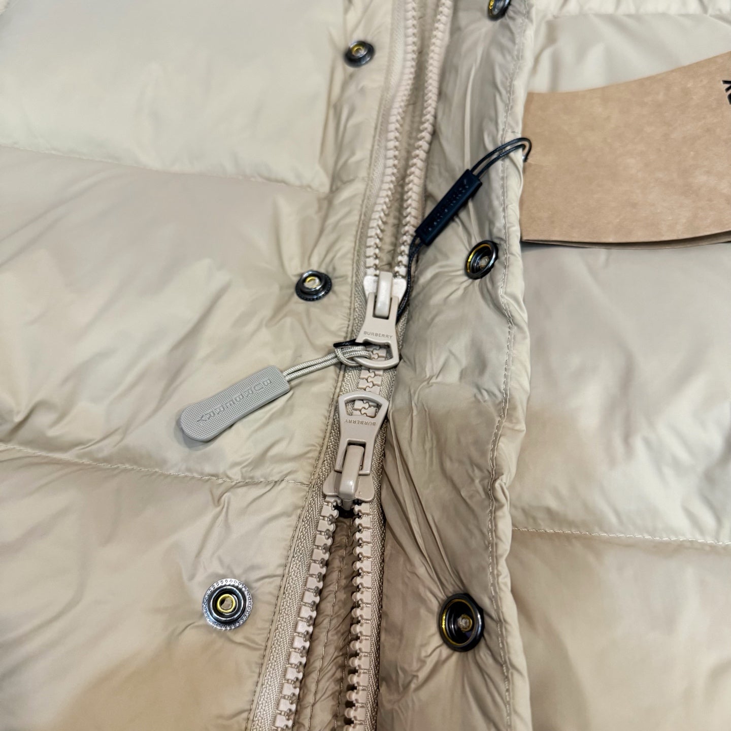 Burberry puffer jacket front, light beige with zip pull, snap buttons, and hardware.