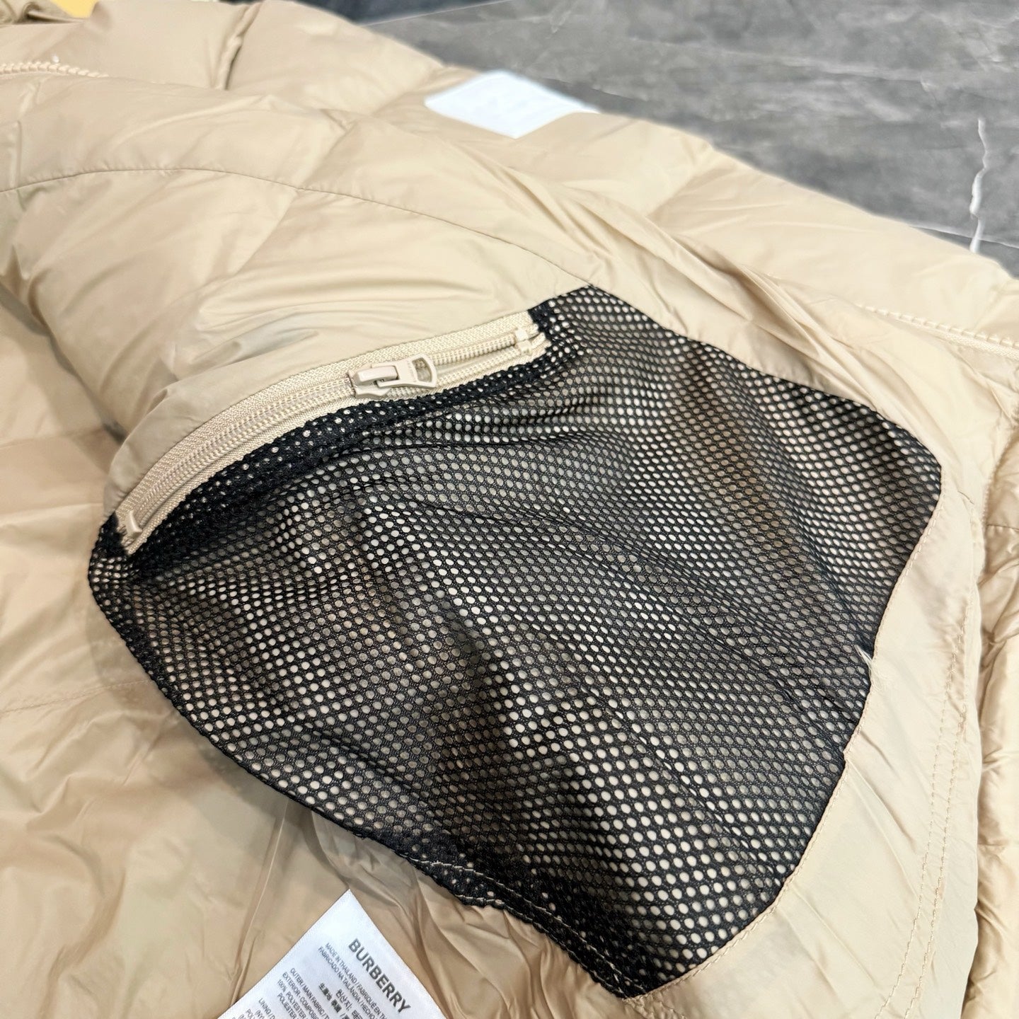 Burberry puffer jacket, light beige with black mesh inner pocket opening.