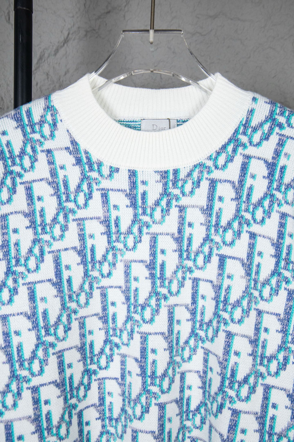 Dior knit sweater close-up: ribbed white crew neck and blue logo pattern