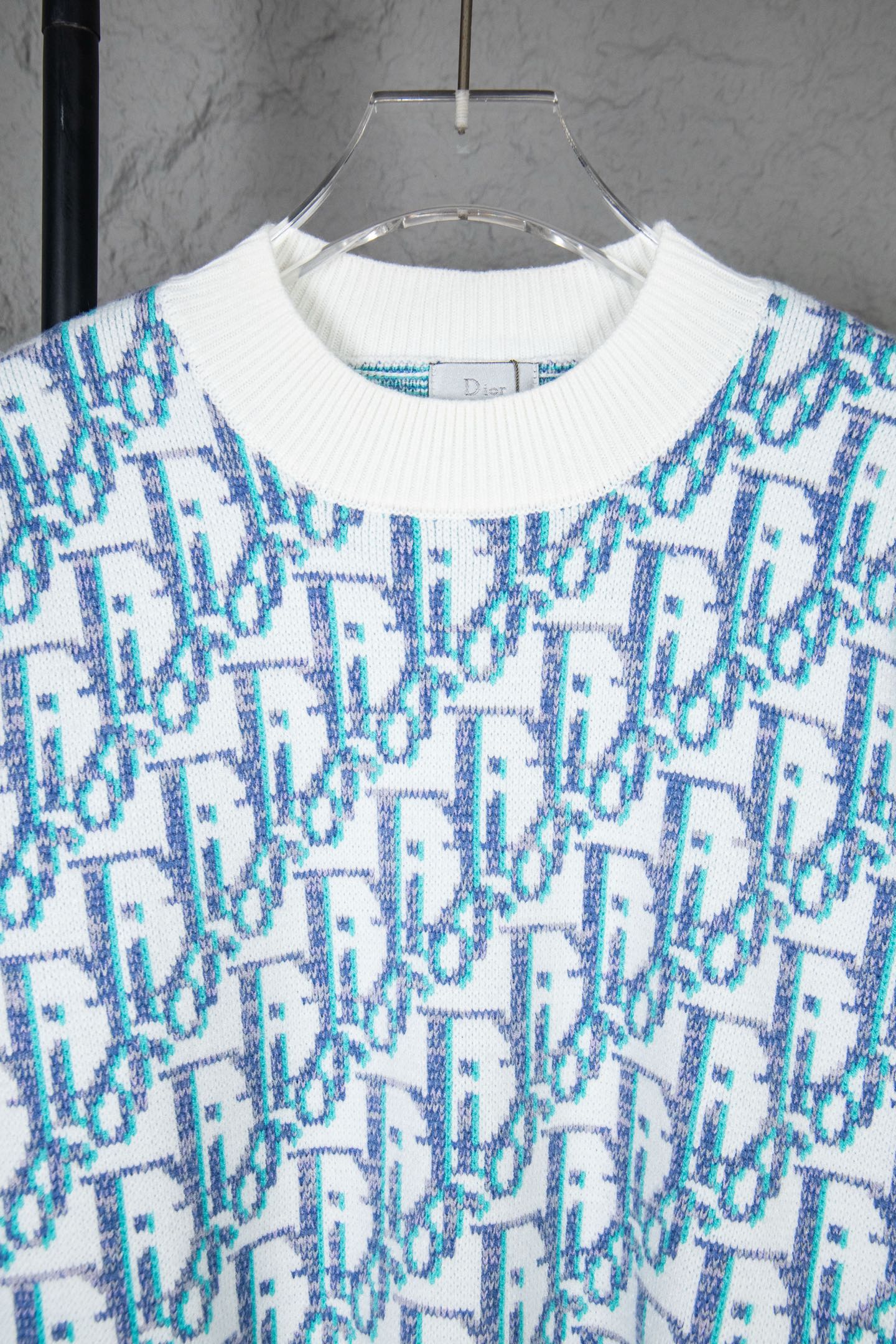 Dior knit sweater close-up: ribbed white crew neck and blue logo pattern
