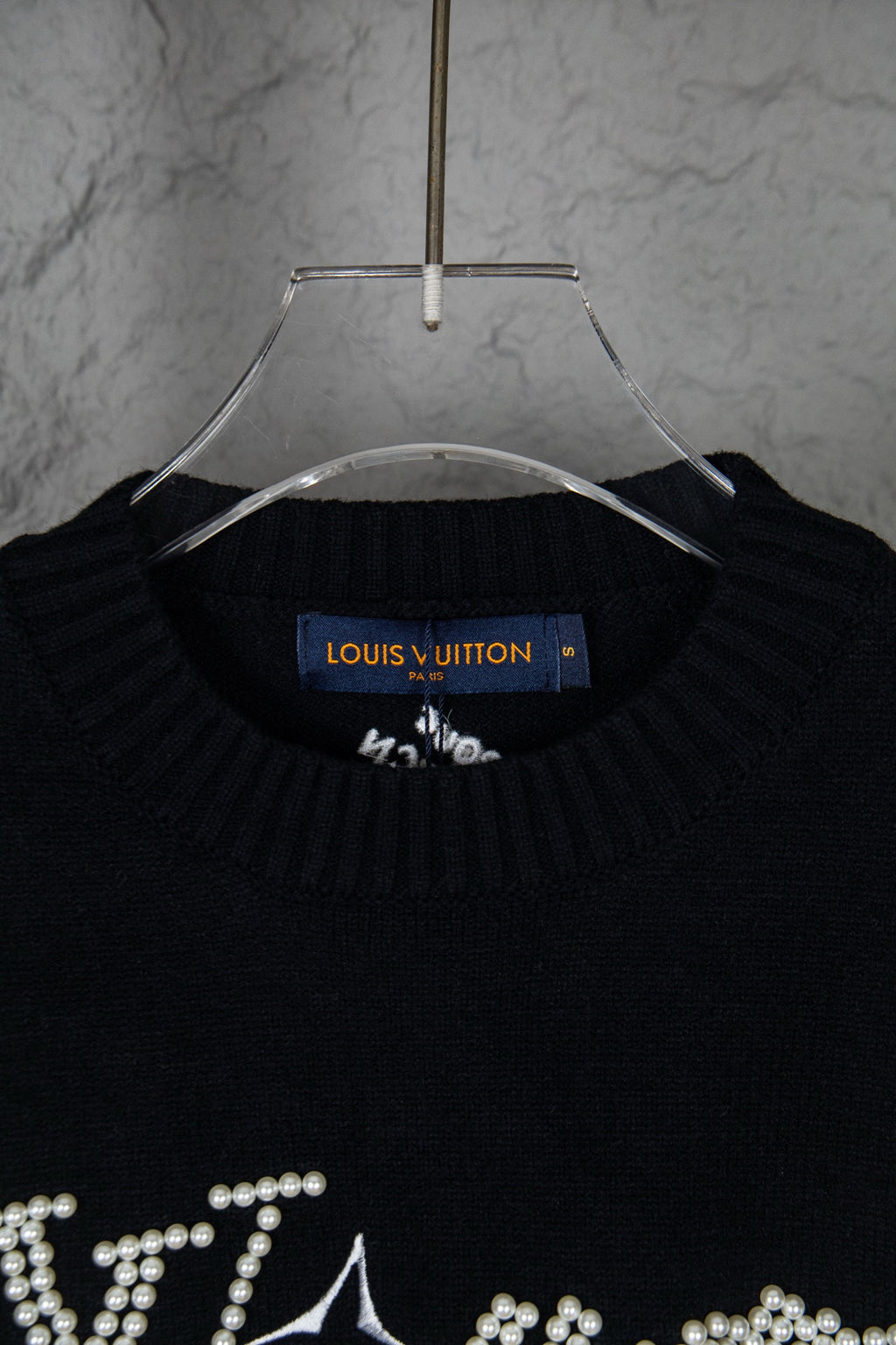 Black knit sweater neckline with blue Louis Vuitton label and rhinestone details