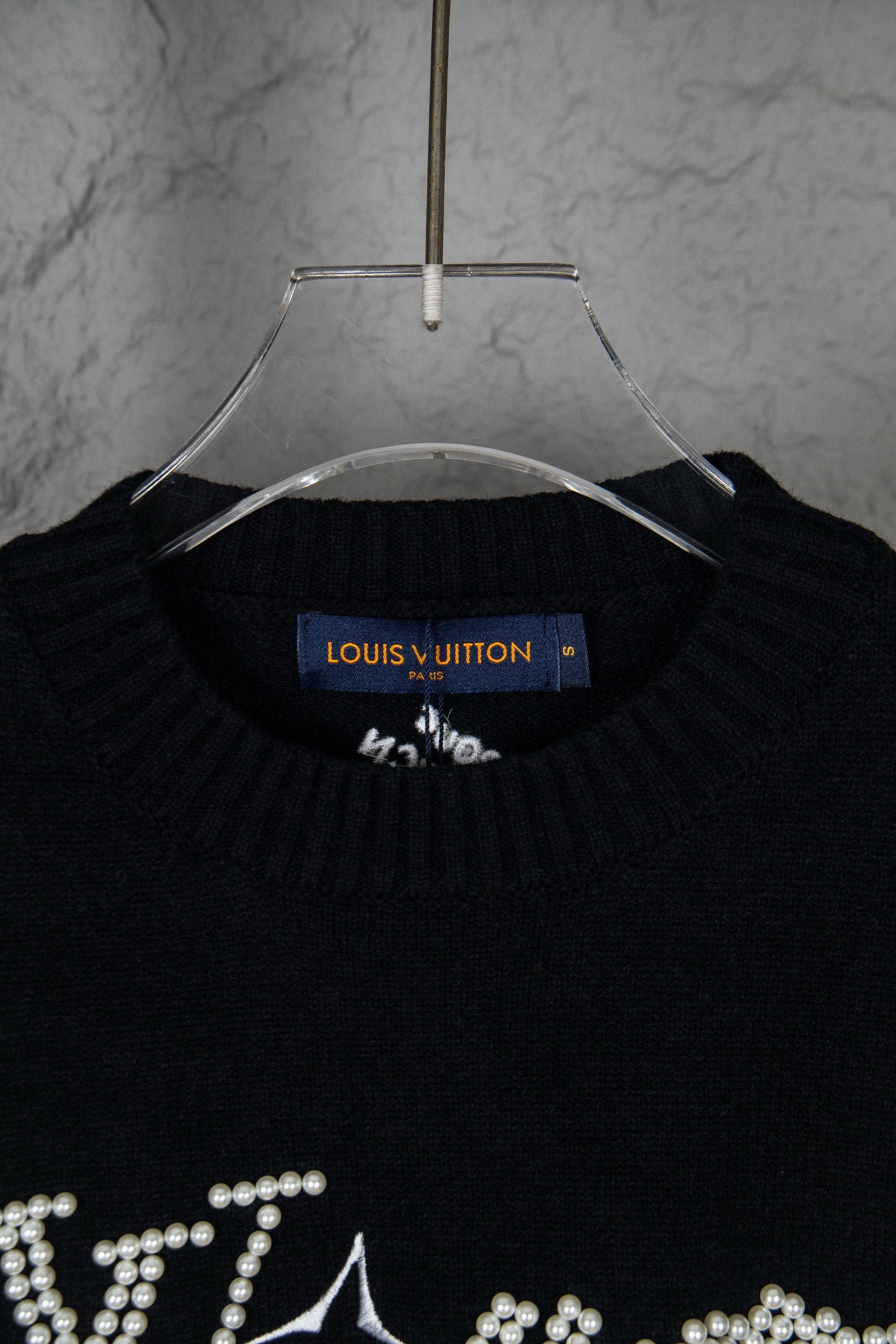 Black knit sweater neckline with blue Louis Vuitton label and rhinestone details