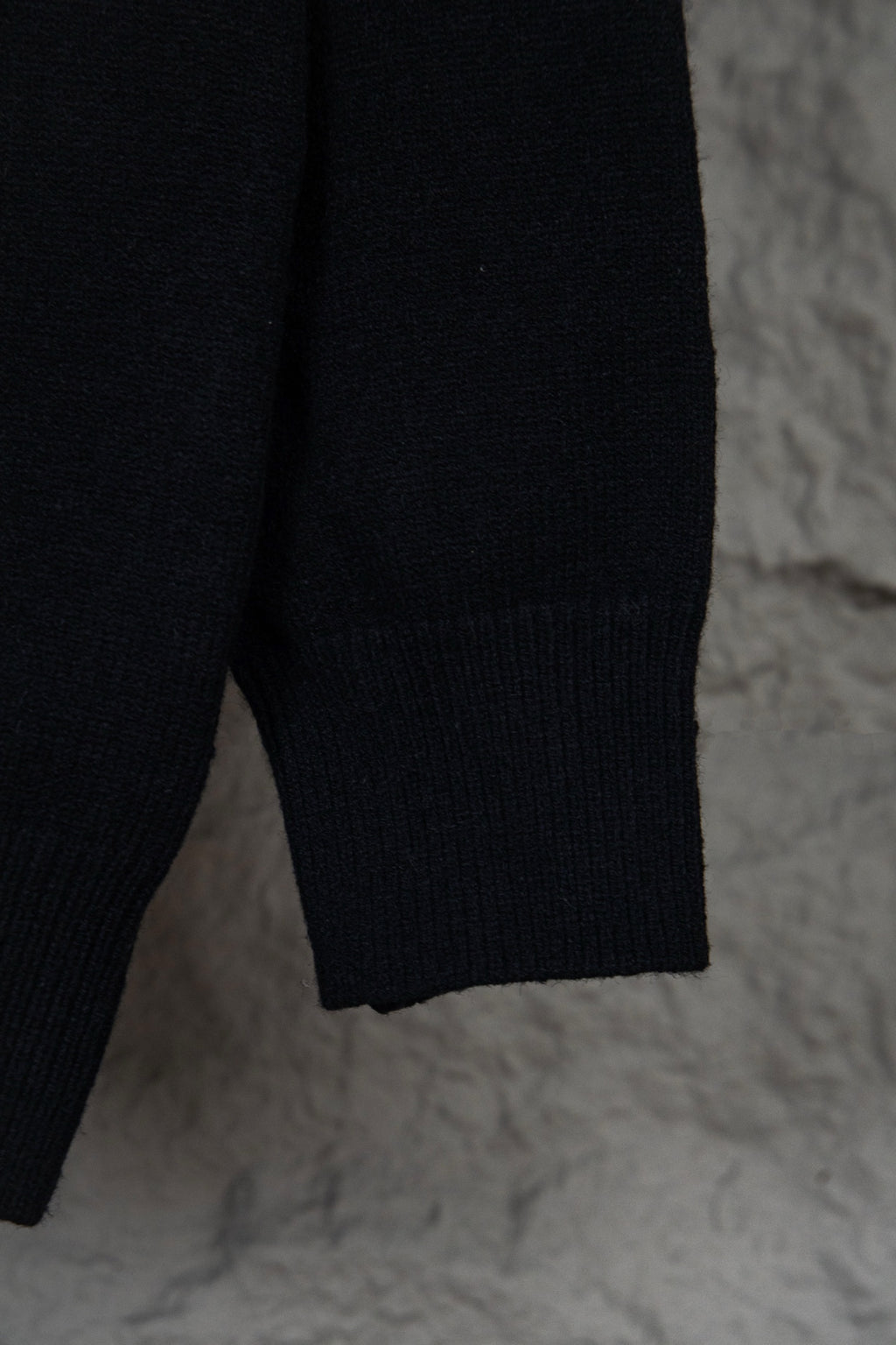 Black long-sleeve knit sweater with small white graphic text on upper back
