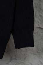 Black long-sleeve knit sweater with small white graphic text on upper back