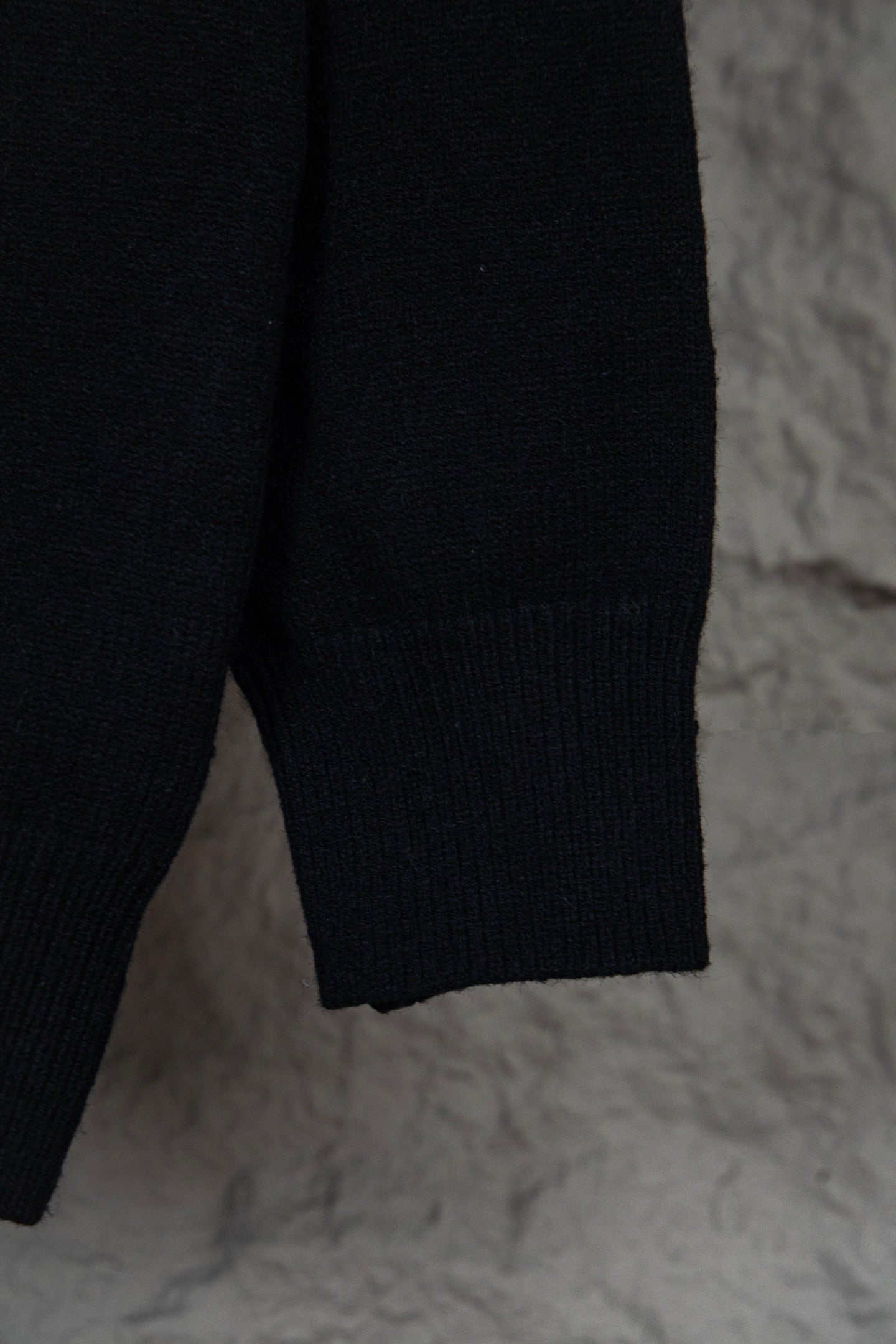 Black long-sleeve knit sweater with small white graphic text on upper back
