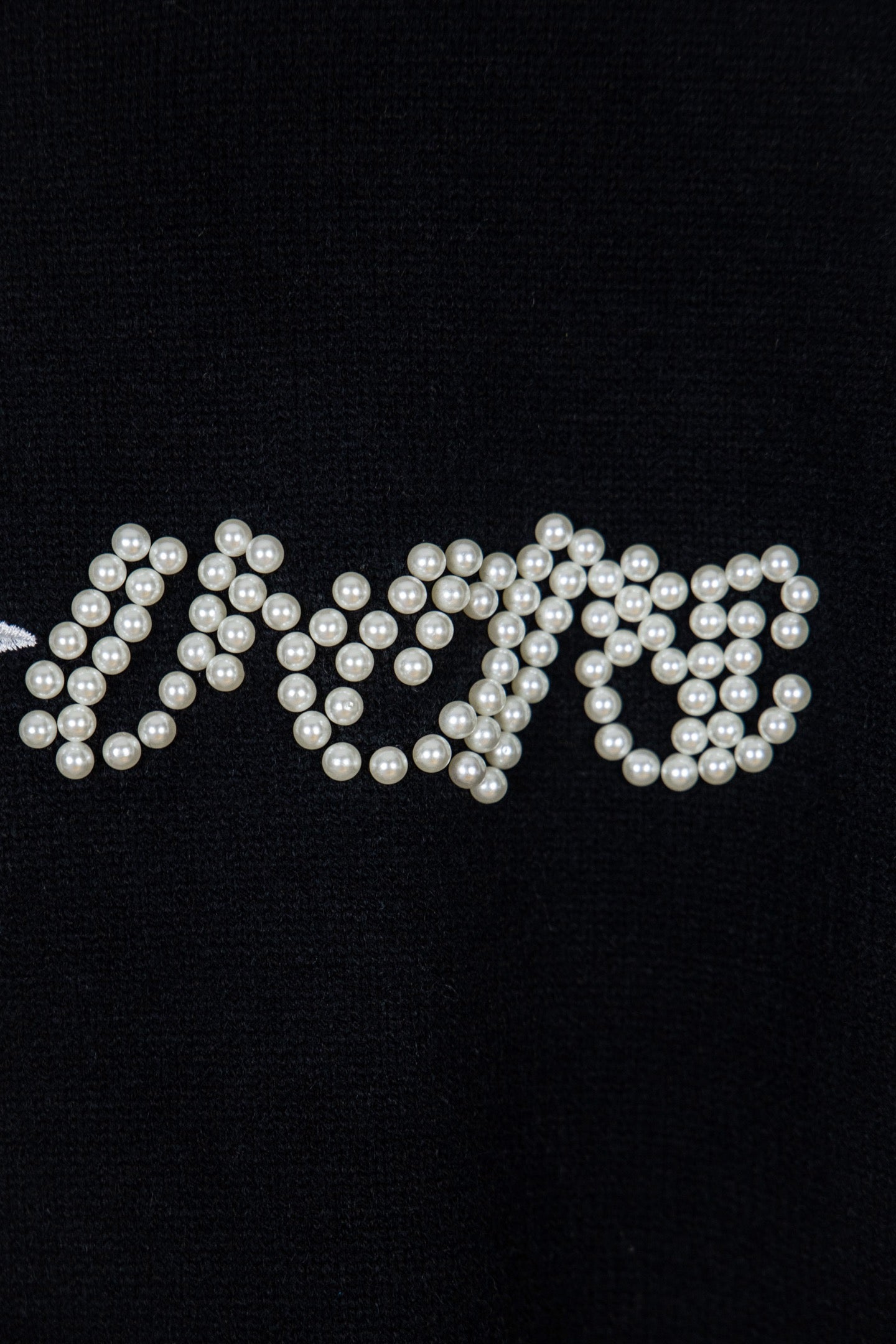 Black knit sweater with pearl-embellished lettering across the chest