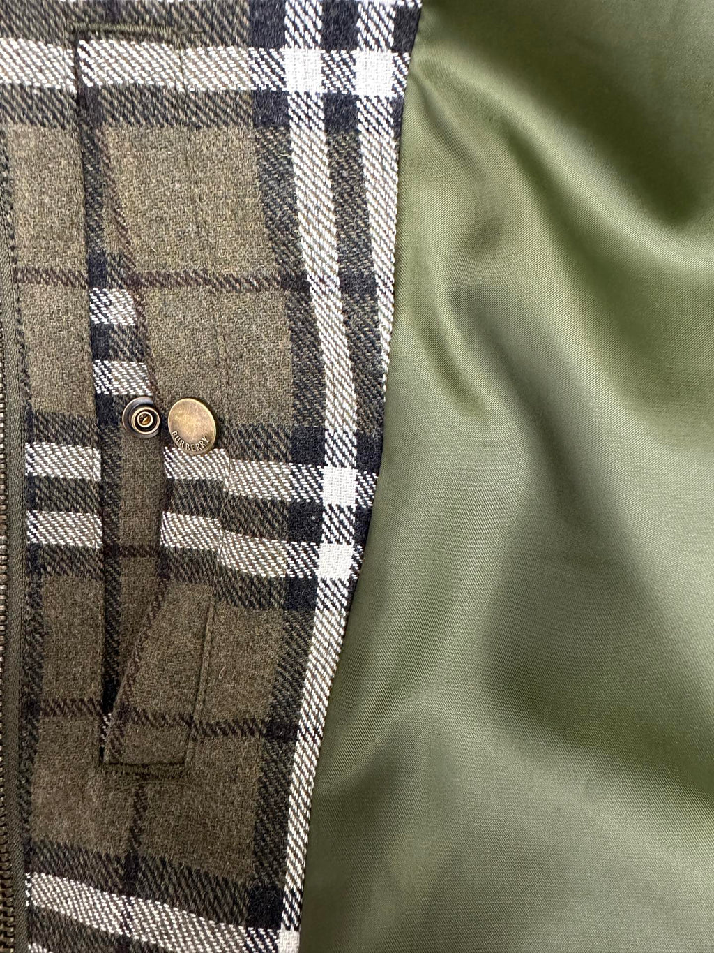 Olive green plaid jacket front with two brass snap buttons and vertical pocket seams