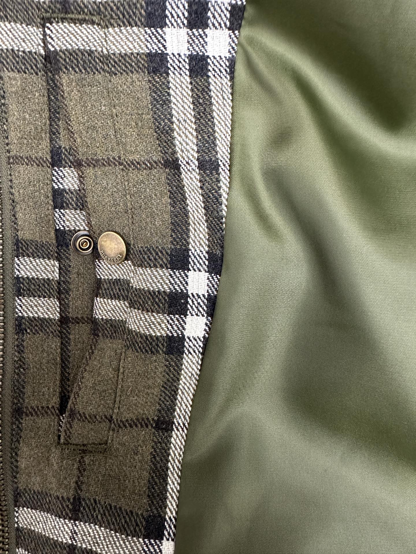 Olive green plaid jacket front with two brass snap buttons and vertical pocket seams