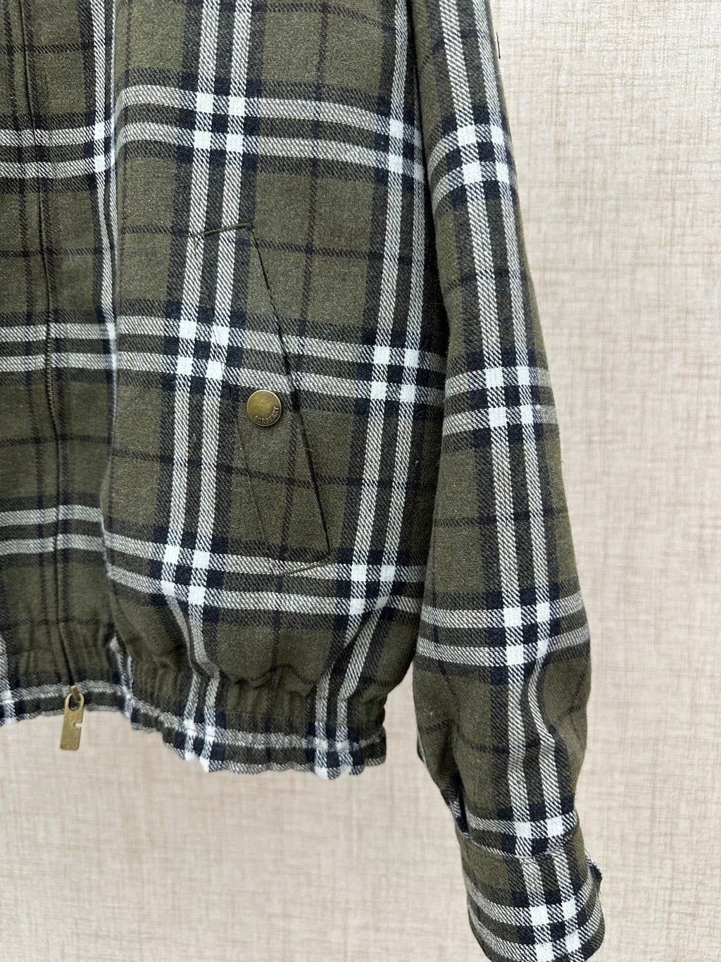 Olive green and black plaid jacket front pocket with brass button and drawstring hem