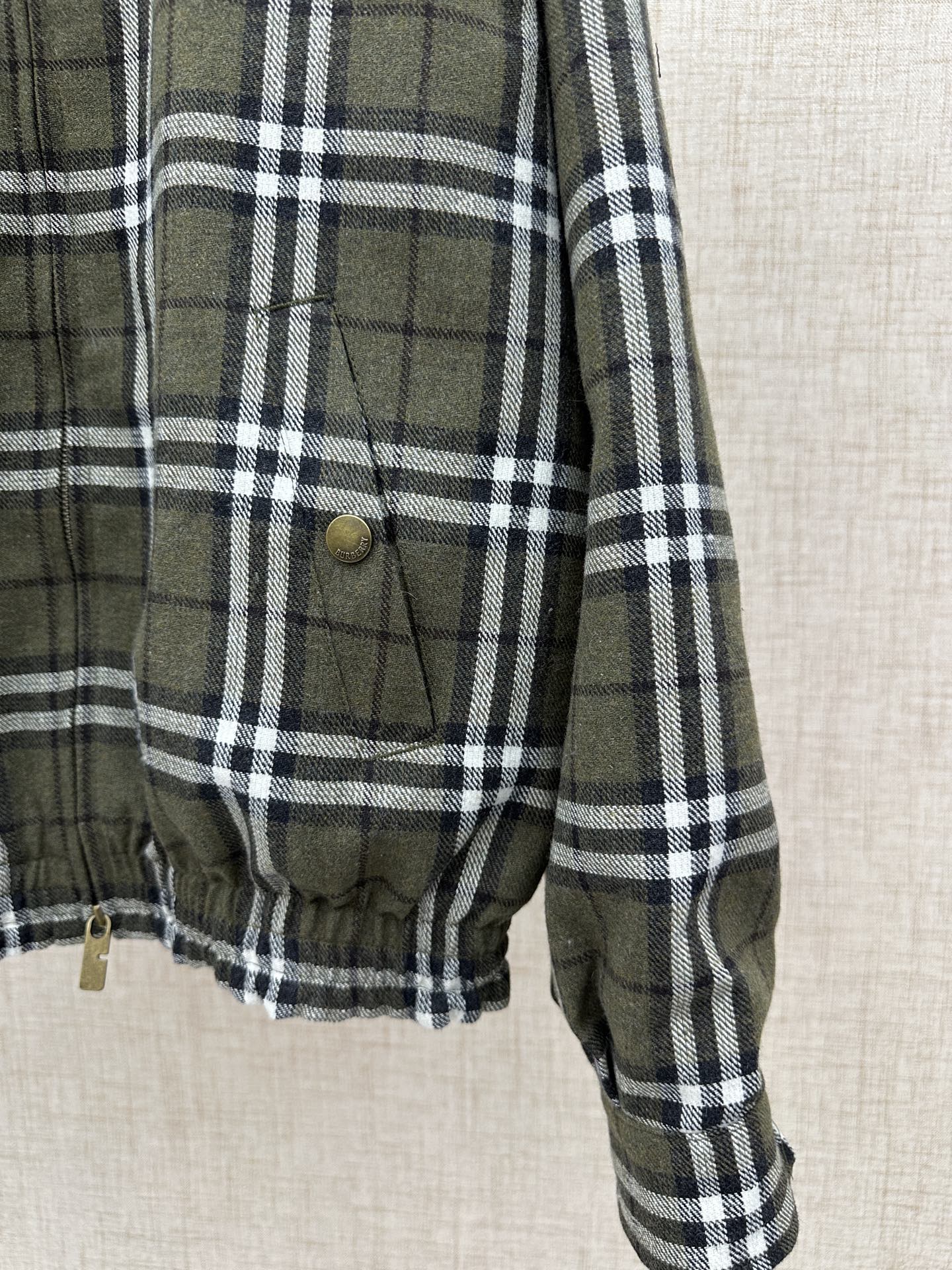 Olive green and black plaid jacket front pocket with brass button and drawstring hem
